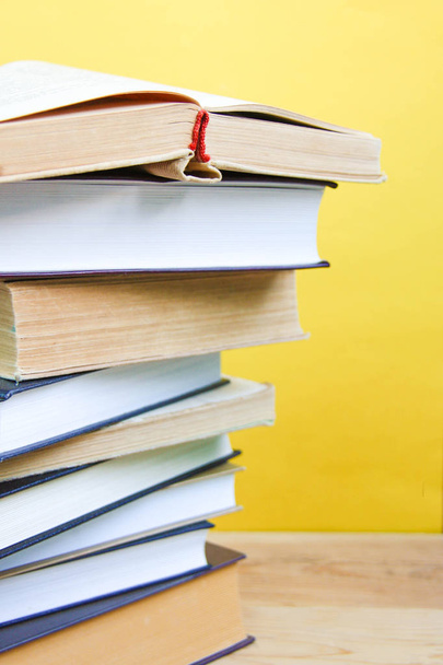 Back to school and knowledge concept. Stack of books on wooden background and trendy yellow wall. Front view - 写真・画像