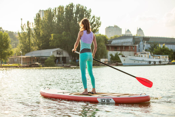 Woman is floating on a SUP board on sunny morning. Stand up paddle boarding - awesome active recreation during vacation. - Foto, imagen