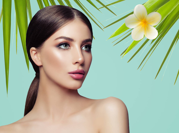 Facial treatment, skincare, wellness and spa. Clear soft skin, healthy face. Portrait of a beautiful girl against a background of tropical leaves and flowers. Spa concept. Natural beauty - Photo, Image