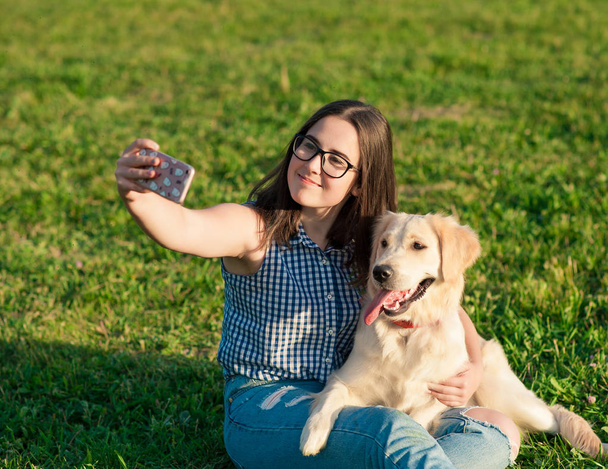 νεαρή γυναίκα και το φιλικό σκυλί λαμβάνοντας μια selfie σε ένα πάρκο - Φωτογραφία, εικόνα