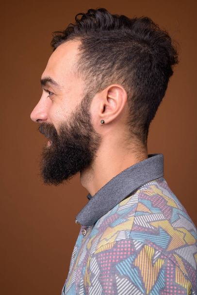 Stúdió lövés fiatal jóképű szakállas perzsa férfi ellen barna háttér - Fotó, kép