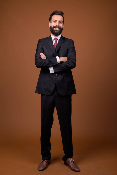 Estudio toma de joven guapo barbudo persa hombre de negocios sobre fondo marrón - Foto, imagen