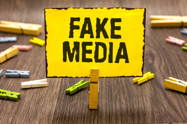 Text sign showing Fake Media. Conceptual photo An formation held by brodcasters which we cannot rely on Clothespin holding yellow paper note several clothespins wooden floor - Photo, Image