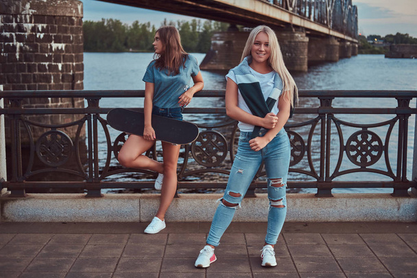 Dvě dívky nádherné bokové s skateboard proti most. - Fotografie, Obrázek