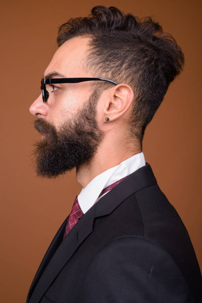 Studio záběr mladý hezký vousatý perský podnikatel nosí dioptrické brýle hnědé pozadí - Fotografie, Obrázek
