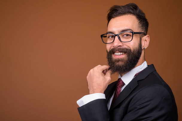 Studio colpo di giovane bello barbuto uomo d'affari persiano indossa occhiali contro sfondo marrone
 - Foto, immagini
