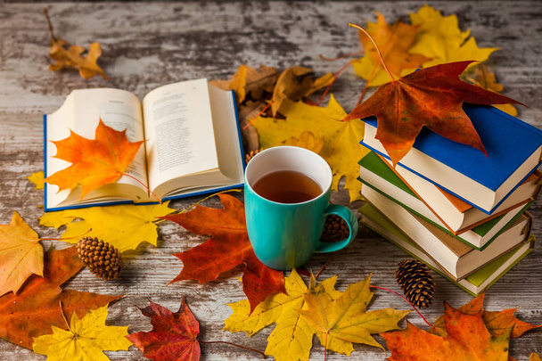 Otoño. Un libro abierto. Una taza de té, café, cacao. Hojas rojas amarillas. Fondo de madera
 - Foto, imagen
