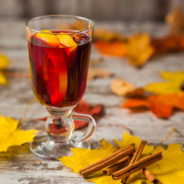 Hot Mulled Wine. On autumn background. Orange Cinnamon Red wine in the glass. Alcohol. Autumn leaves Yellow red. On wooden dark background. - Photo, Image