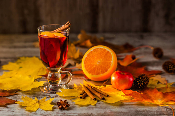 ホットホット ワイン。秋の背景。グラスにオレンジ シナモン赤ワイン。アルコール。紅葉は黄色赤い。木製の暗い背景に. - 写真・画像