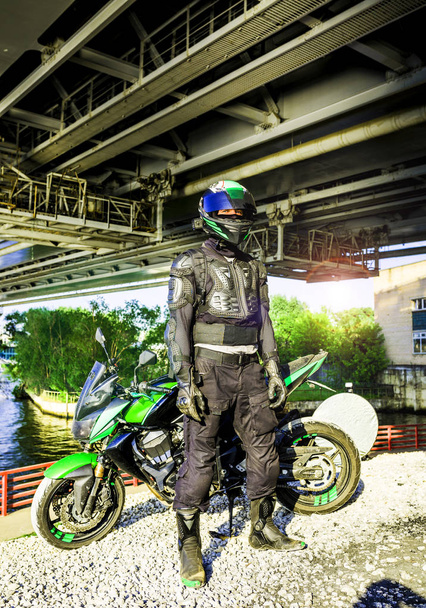 μοτοσικλετιστής σε ένα κράνος και προστατευτικό ρουχισμό που στέκεται κάτω από τ - Φωτογραφία, εικόνα