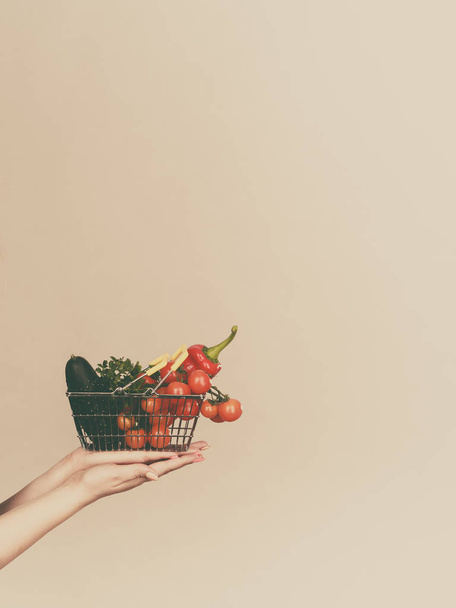 Потерять вес, покупать здоровую пищу, вегетарианские продукты. Рука держит корзину с овощами, на сером
 - Фото, изображение