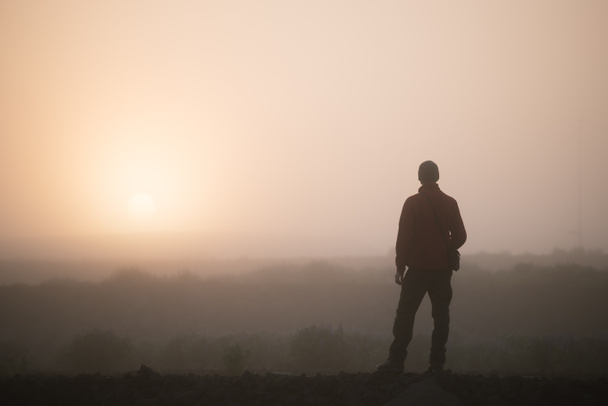 Man thinks looking at the rising sun. Morning landscape with fog - Photo, Image