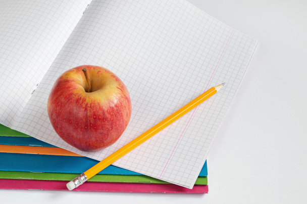 Lápiz y manzana encima del cuaderno de la escuela sobre fondo blanco. El tema de la educación
 - Foto, Imagen