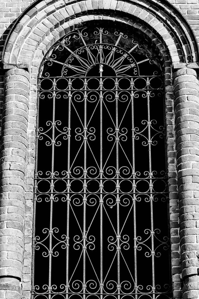 Gebogen venster met smeedijzeren staven in de oude kerk - Foto, afbeelding