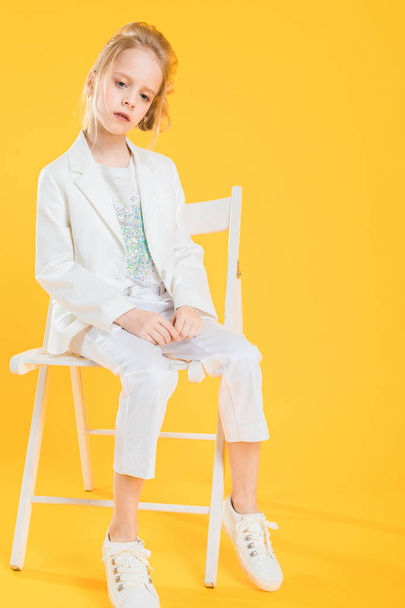 Una adolescente vestida de blanco está sentada en una silla sobre un fondo amarillo
. - Foto, imagen