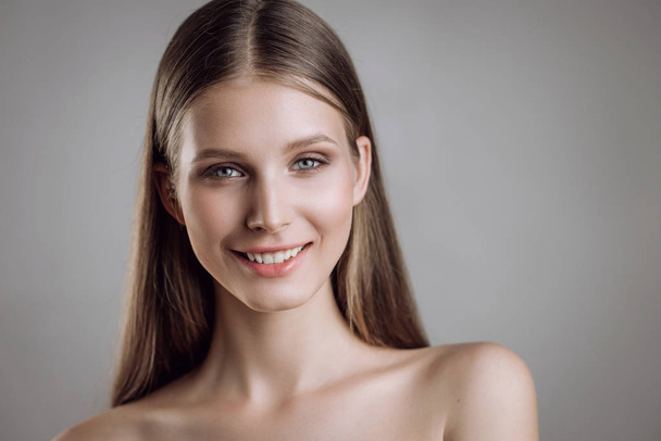 Portrait of a beautiful young girl with nude make-up in studio on a gray background - Foto, Imagen