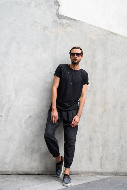 Handsome man wearing sunglasses against concrete wall in the str - Foto, Bild
