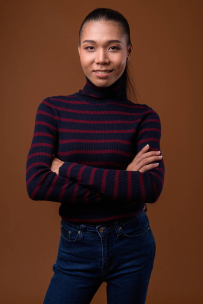 Молодая красивая азиатская трансгендерная женщина на коричневом фоне
 - Фото, изображение