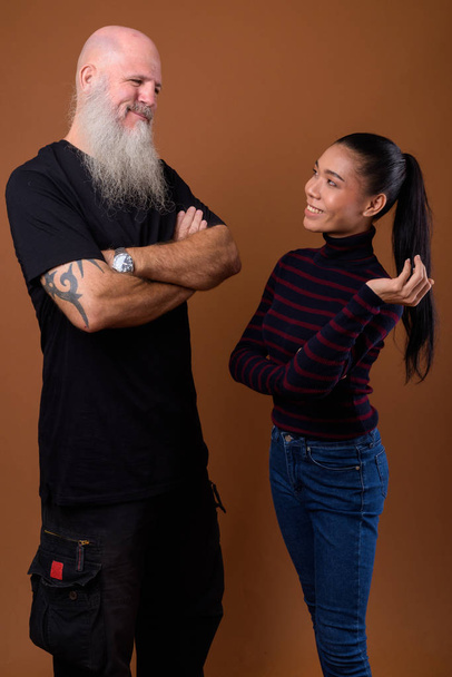 Зрелый бородатый лысый мужчина с молодой азиатской трансгендерной женщиной
 - Фото, изображение