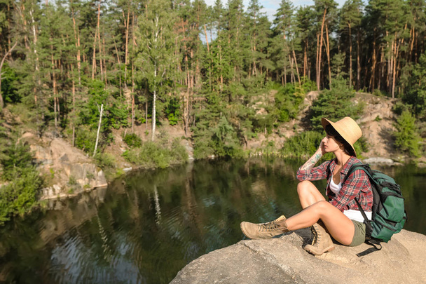 Young woman on rock near lake and forest. Camping season - Foto, Bild