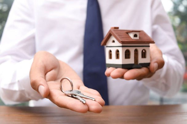 Real estate agent holding house model and keys at table - Foto, Bild