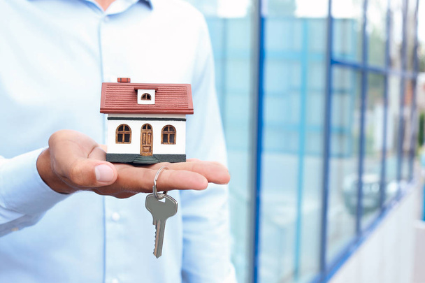 Агент по недвижимости держит модель дома и ключ на размытом фоне
 - Фото, изображение