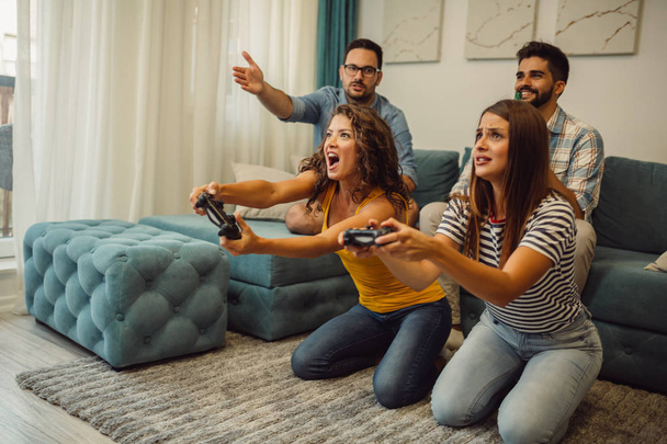 Ποιος θα κερδίσει; Ενθουσιασμένος φίλοι παίζουν βιντεοπαιχνίδια σε κλειστούς χώρους στο σπίτι. - Φωτογραφία, εικόνα