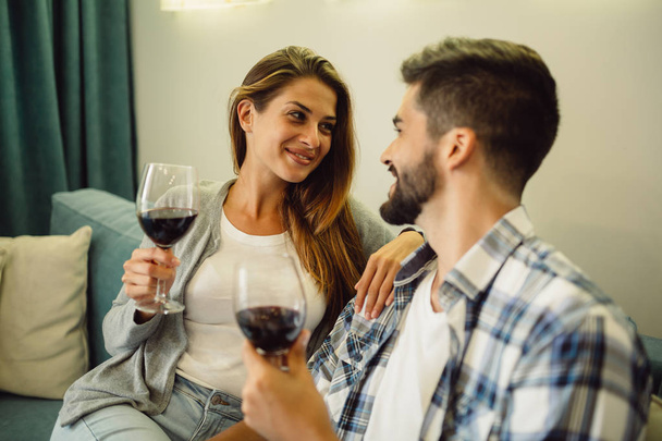 Portret uśmiechający się młoda para obchodzi rocznicę z kieliszków wina w domu na kanapie - Zdjęcie, obraz