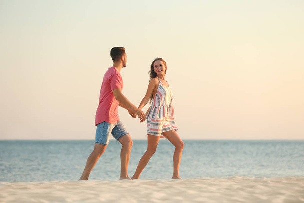 Happy young couple walking together on beach - Φωτογραφία, εικόνα