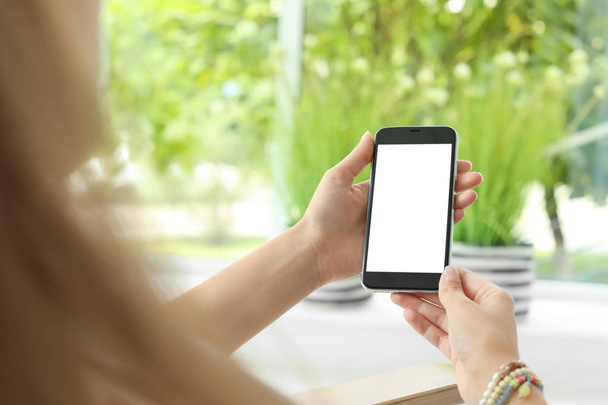 Woman holding smartphone with blank screen on blurred background. Mockup for design - Fotoğraf, Görsel