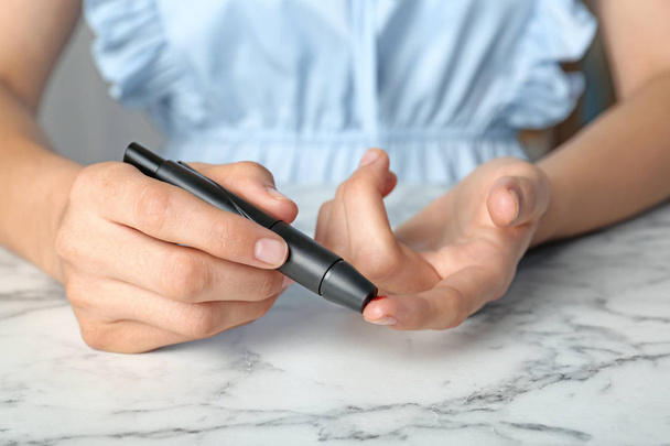 Woman using lancet pen at table. Diabetes test - Fotoğraf, Görsel