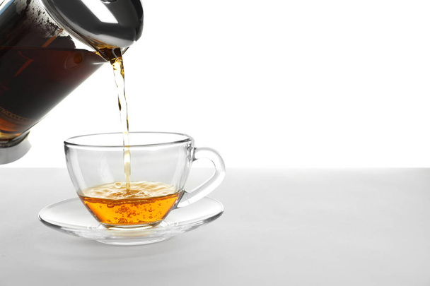 Pouring hot tea into glass cup on white background - Foto, Bild