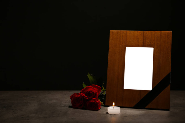 Empty frame with black ribbon, candle and roses on table. Funeral symbol - Fotografie, Obrázek
