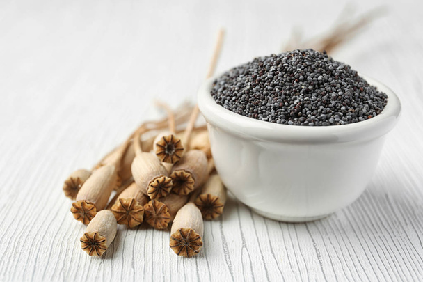 Dry poppy heads and bowl with seeds on white wooden background - Zdjęcie, obraz