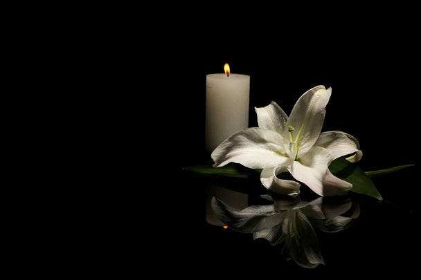 Beautiful lily and burning candle on dark background with space for text. Funeral flower - Φωτογραφία, εικόνα