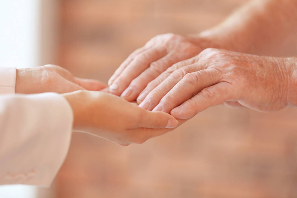 Young woman holding elderly man hands indoors, closeup. Help service - Photo, Image