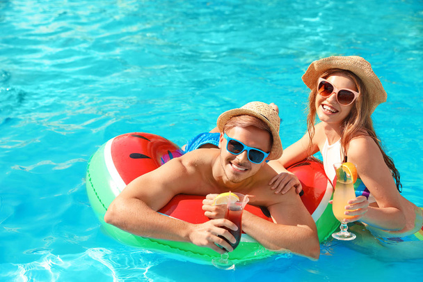 Young couple with cocktails in pool on sunny day - Φωτογραφία, εικόνα