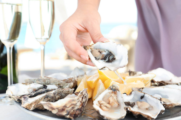 Woman holding fresh oyster over plate, focus on hand - Foto, imagen