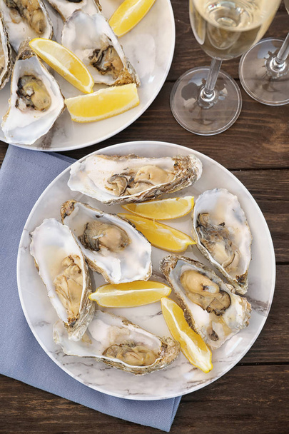 Fresh oysters with cut juicy lemon served on table, flat lay - Foto, afbeelding