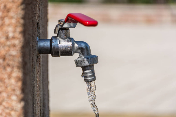 Faucet with red handle and open water outdoor on sunny summer day. Save water concept. Close up, selective focus - Foto, Imagen