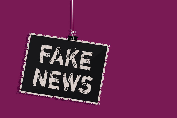 Γράφοντας κείμενο λέξη Fake News. Επιχειρηματική ιδέα για την παροχή πληροφοριών στους πολίτες ότι δεν είναι αλήθεια από μέσα κρέμονται μαυροπίνακα μήνυμα επικοινωνίας πληροφορίες σύμβολο μωβ φόντο - Φωτογραφία, εικόνα