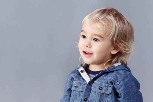 Portrait of a young blond boy on gray background. A three years boy looks into the distance - Foto, Bild