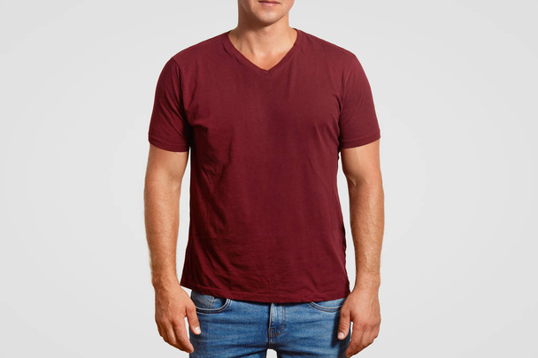 Indoor cropped image of muscular young man in red t shirt and jeans, stands against white background, poses over white background, blank space or your logo or advertisement. Clothing concept - Fotoğraf, Görsel