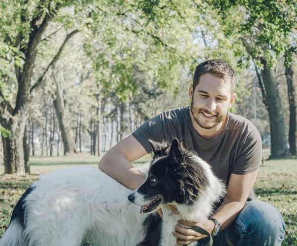 Homem com seu cão brincando ao ar livre no parque. Jovem proprietário abraça seu animal de estimação na natureza
. - Foto, Imagem