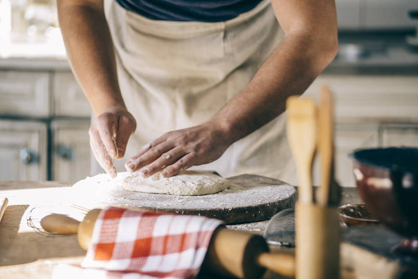 Man kneading and baking homemade pizza dough in the kitchen. Closeup on baker's hands preparing loaf of bread. Cooking and food preparation at home. - Photo, image