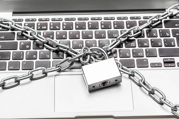 Closed laptop computer with chain wrapped around it and padlocked - 写真・画像