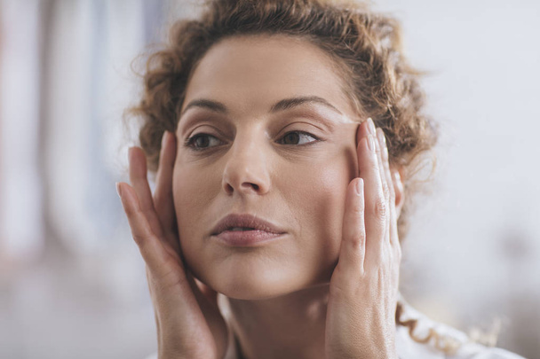 Beautiful Caucasian woman applying face cosmetic cream on her face. - Valokuva, kuva