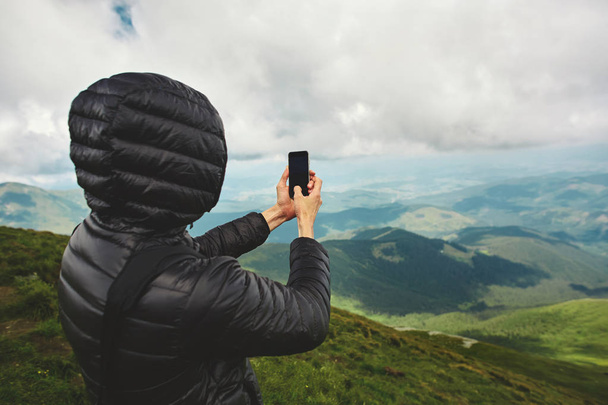 active hiker enjoying panoramic view of cloudy sunrise in mountains and taking photos by the phone on mountain ridge. travel and outdoor adventure concept. Carpathians, Ukraine - Фото, изображение