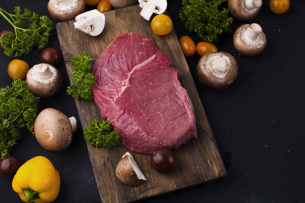 Steak meat on a black background. Beef and vegetables and mushrooms for cooking dinner. Free space for text. Top view. - 写真・画像