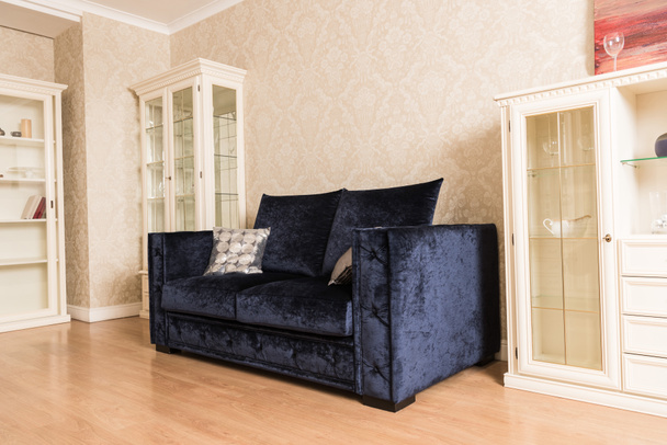 interior da sala de estar com sofá azul, prateleiras de madeira e piso
 - Foto, Imagem